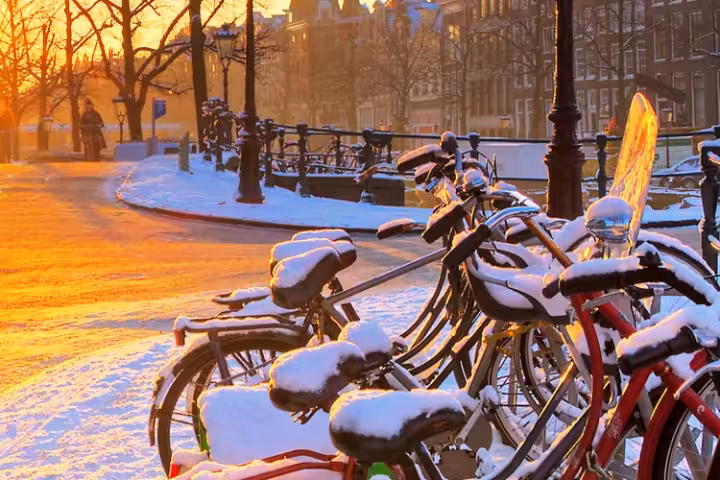 Bicicletas cobertas de neve ao lado de um canal de Amsterdã ao nascer do sol