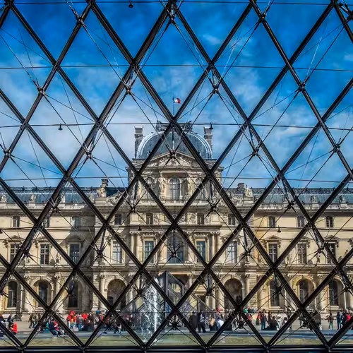 The Louvre palace seen through the glass and steel frame of the Pyramid, with visitors in the courtyard