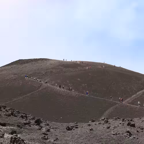 Des randonneurs marchent en file indienne sur un versant sombre recouvert de cendres volcaniques de l'Etna.