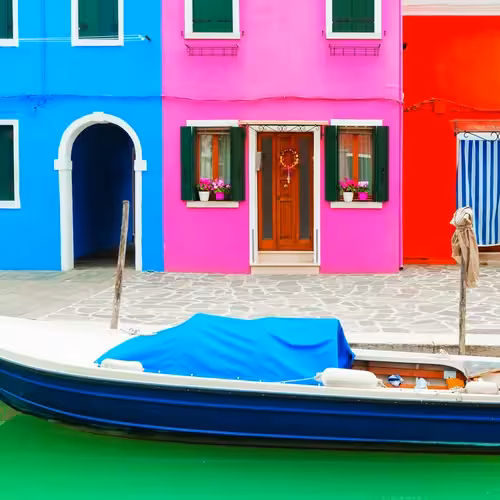Maisons bleues, roses et rouges au bord d'un canal avec un bateau amarré à Burano