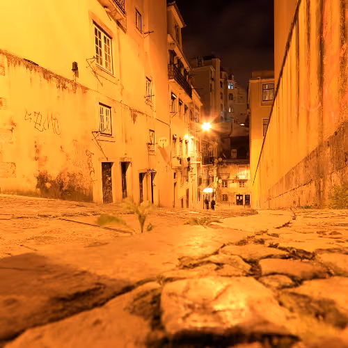 Un'affascinante e stretta via di Almada, in Portogallo, illuminata da calde luci di lampioni, che mette in risalto l'architettura storica e l'atmosfera invitante della regione di Lisbona di notte.