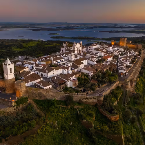 Una vista mozzafiato del lago di Alqueva al tramonto, che mette in risalto le acque tranquille e il pittoresco villaggio nella regione dell'Alentejo, in Portogallo.