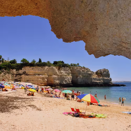 Persone che si godono una giornata di sole in spiaggia con ombrelloni colorati e splendide scogliere ad Armação de Pêra, Algarve, Portogallo.