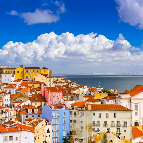 I tetti colorati di Alfama, a Lisbona, con la cupola bianca del Pantheon Nazionale e il fiume Tago sullo sfondo.