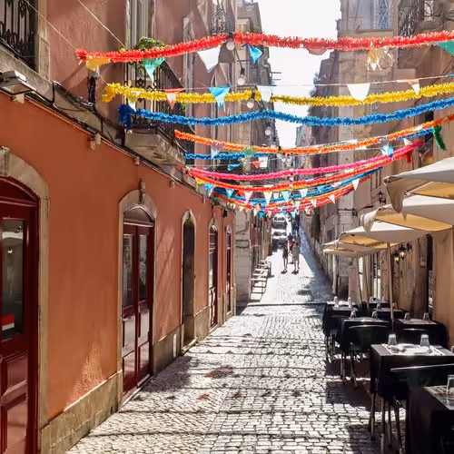 Stretta via acciottolata nel Bairro Alto di Lisbona, decorata con colorate ghirlande di carta e ombrelloni da caffè.