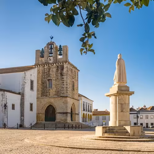 The bell tower of Faro Cathedral and a statue in the cathedral square, in the old town of Faro, Algarve.