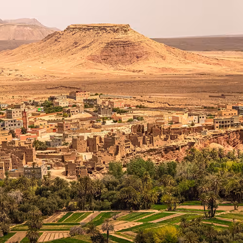Vista panorámica de Boumalne Dades en Drâa-Tafilalet, Marruecos, con colinas desérticas, edificios tradicionales de estilo kasbah y un exuberante oasis de palmeras en el valle del Dades.