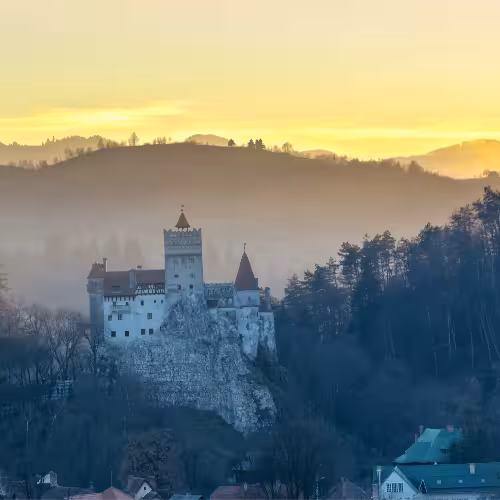 Castelo de Bran ao entardecer, com as colinas ao fundo.