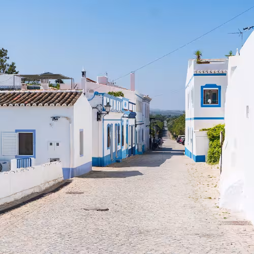 Charming whitewashed buildings with blue accents line a quaint street in the picturesque village of Cacela Velha in the Algarve region of Portugal.