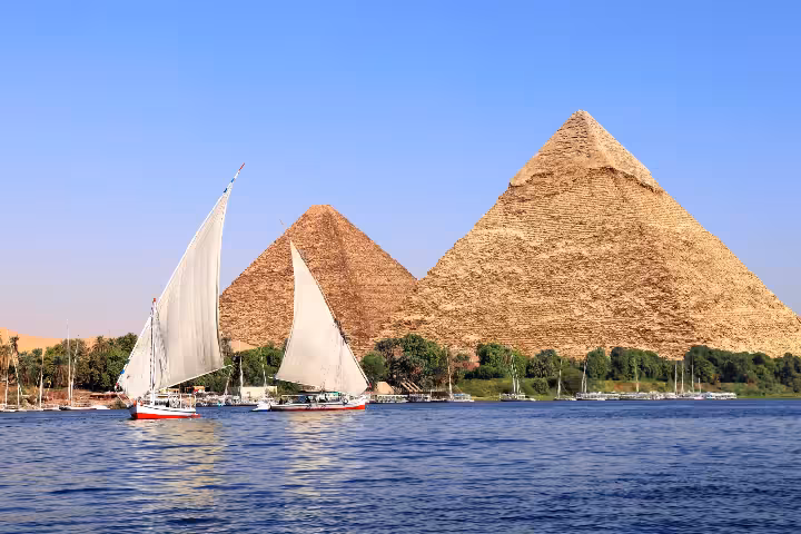 Traditional felucca sailboats cruising the Nile River with the iconic Pyramids of Giza in the background during a guided Cairo tour experience in Egypt.
