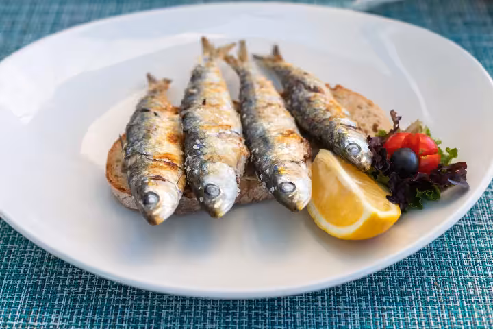 Traditional Algarve grilled sardines served on rustic bread with fresh lemon, tomatoes, olives, and mixed greens, a must-try dish on Algarve food and culinary tours in 2026.