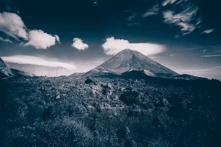 A dramatic black-and-white panoramic view of Pico do Fogo volcano in Cape Verde, showcasing its rugged lava fields and towering volcanic peak under a cloudy sky, ideal for adventurous volcano hiking trails.