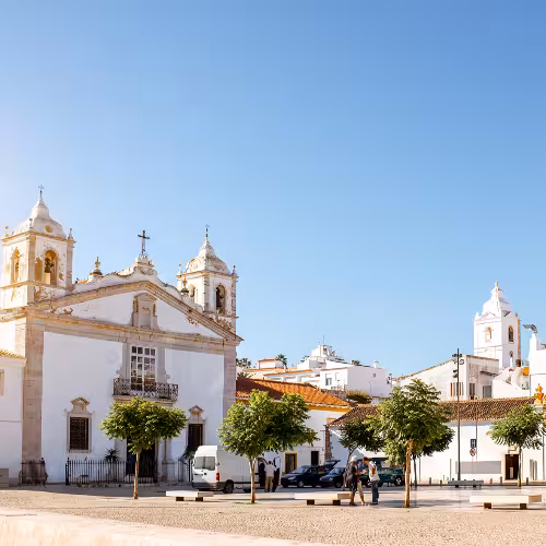 Arquitetura histórica e uma estátua cultural no coração de Lagos, Algarve, Portugal, sob um céu azul límpido.
