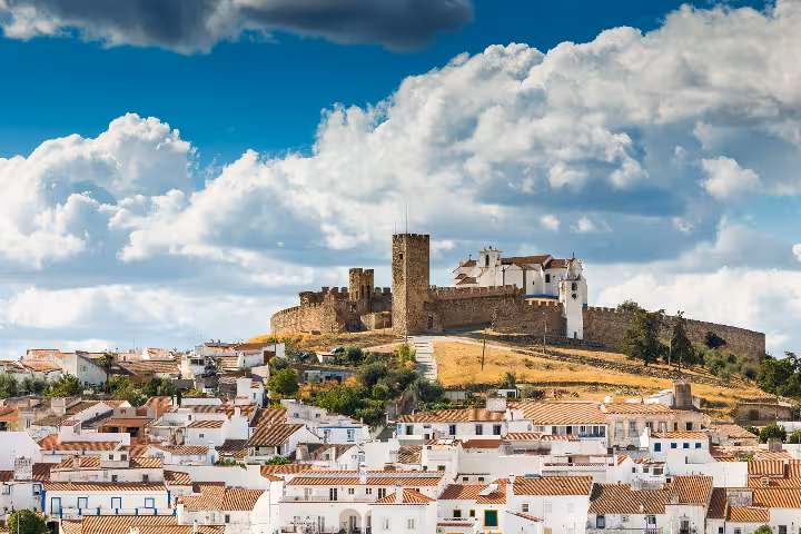 Panoramic view of a historic medieval castle and white church atop a hill overlooking the charming terracotta-roofed village of Arraiolos in the Alentejo region of Portugal, a hidden gem destination that feels like home for travelers exploring authentic P