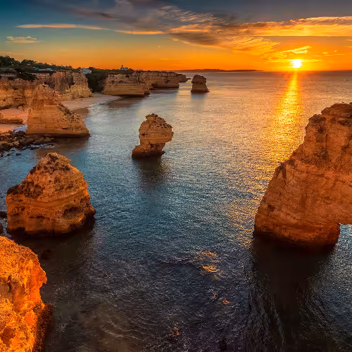 Breathtaking sunset view over the stunning cliffs and turquoise waters at Praia da Marinha, Algarve, Portugal.