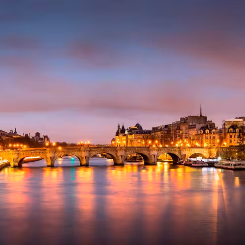 Sunset view of the Seine River and Pont Neuf in Paris, Île-de-France, with glowing city lights and reflections, a top sightseeing spot for Seine river cruises and romantic evening walks.