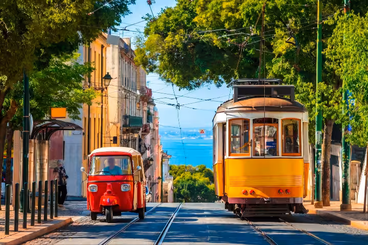 A vibrant Lisbon street scene featuring the iconic yellow tram and a red tuk-tuk navigating the historic cobblestone roads, perfect for exploring private tours vs group tours in Lisbon with ToursXplorer.