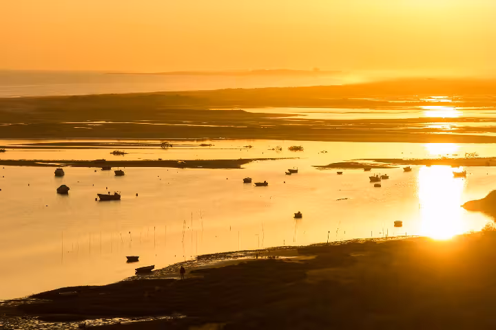 Golden sunset over Ria Formosa Natural Park lagoon in Algarve Portugal with silhouetted fishing boats reflecting on calm shallow waters of this UNESCO protected coastal wetland paradise.