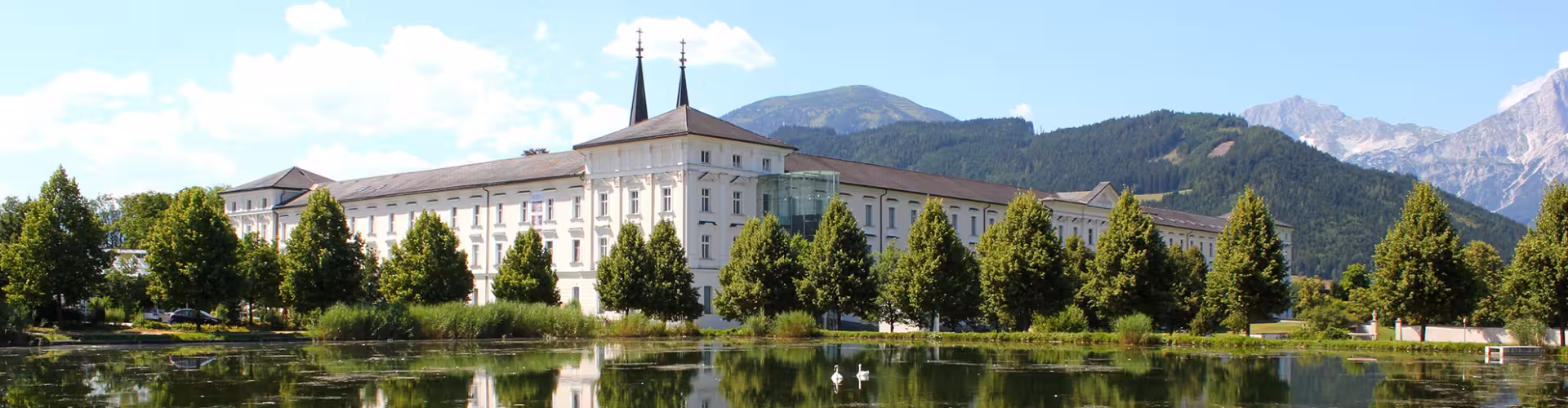 Admont Abbey (Stift Admont) reflected in a tranquil lake with the Gesäuse mountains in Styria, Austria, on a sunny day