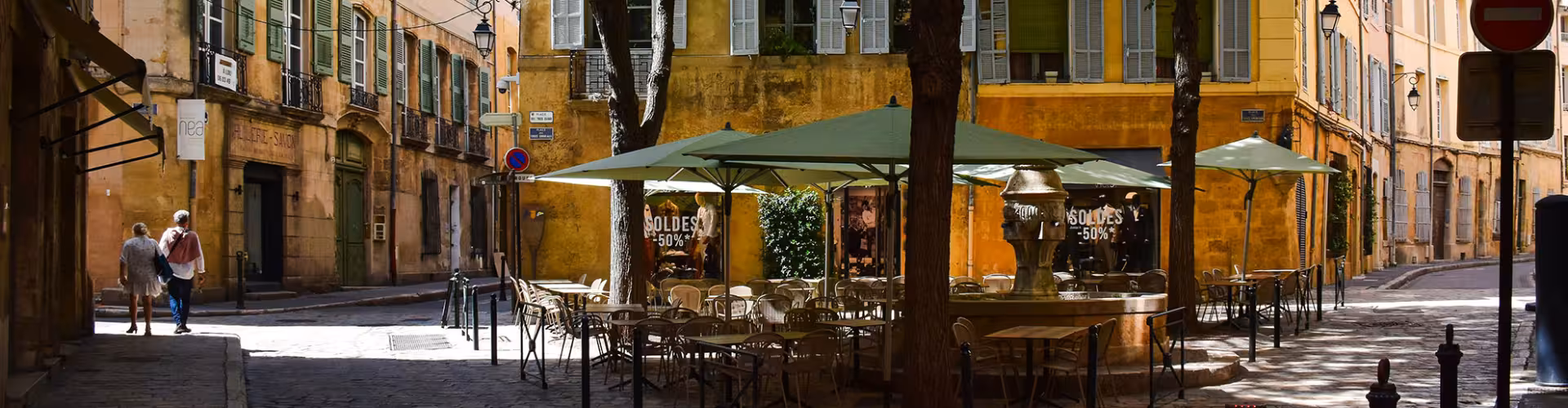 Charming street scene in Aix-en-Provence featuring a quaint café with outdoor seating, historic buildings, and sunlit cobblestone pathways.