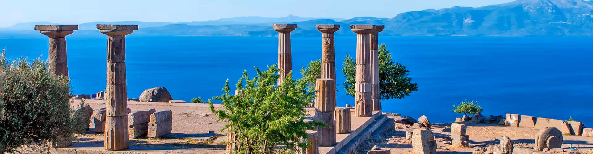 Ancient ruins of Troy featuring towering stone columns overlooking the stunning blue Aegean Sea with scenic mountain backdrop in Çanakkale Turkey UNESCO World Heritage Site.