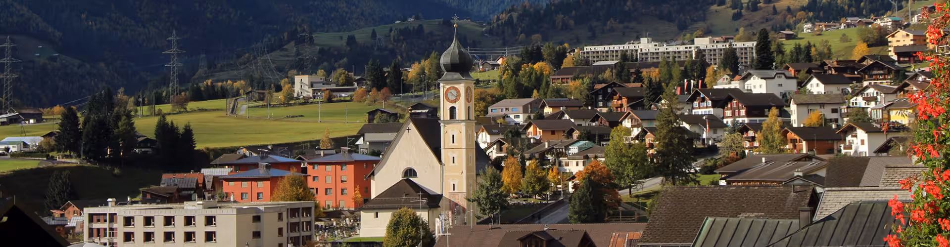 Panoramic view of Disentis, Graubünden, Switzerland, featuring the village church tower, traditional alpine chalets and autumn mountain scenery near the Disentis-Sedrun ski area.
