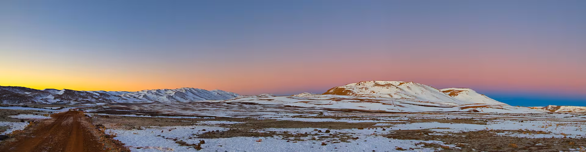 Sunset over snow-covered Atlas Mountains near Ifrane, Morocco, with a scenic road through the Middle Atlas winter landscape.