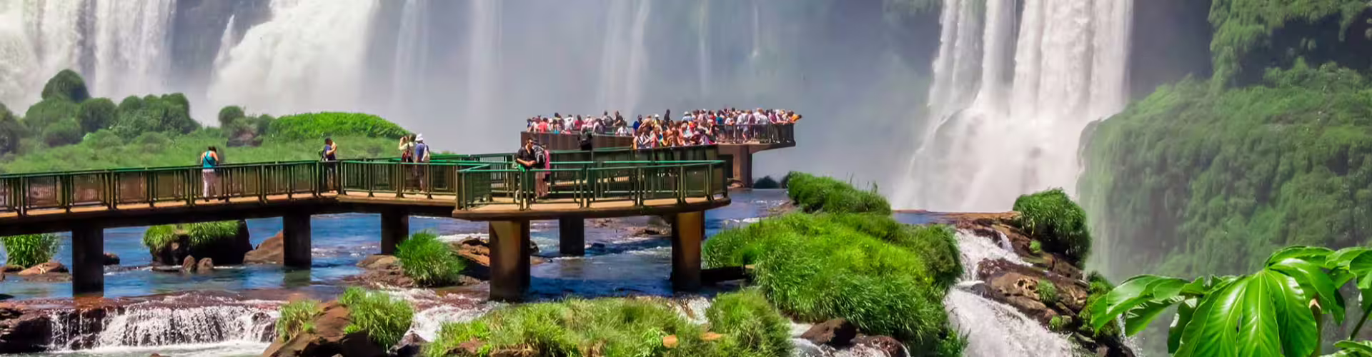 Spectacular view of tourists on a scenic walkway at Iguazu Falls, surrounded by lush greenery and cascading waterfalls in South America.
