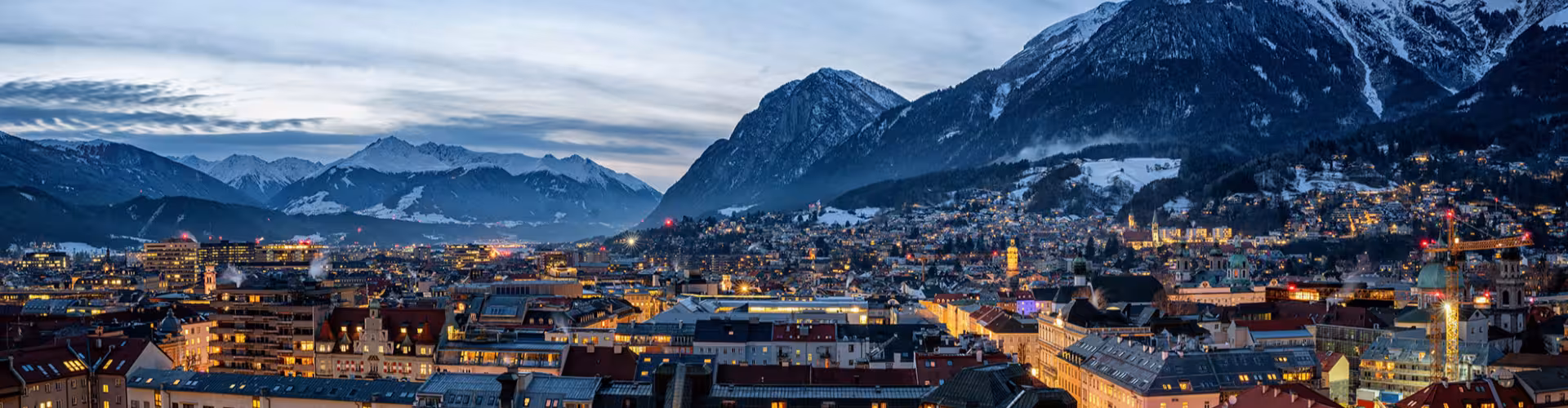 Twilight panorama of Innsbruck in Tyrol, Austria, with glowing Old Town rooftops and the snow-capped Alps—ideal for Tyrol city breaks, winter holidays and Alpine escapes.