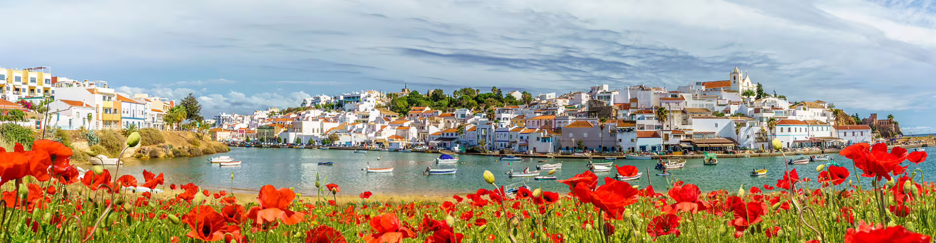 Colorful coastal town of Lagoa in Algarve, Portugal, with vibrant red poppies and traditional whitewashed architecture along the serene waterfront.