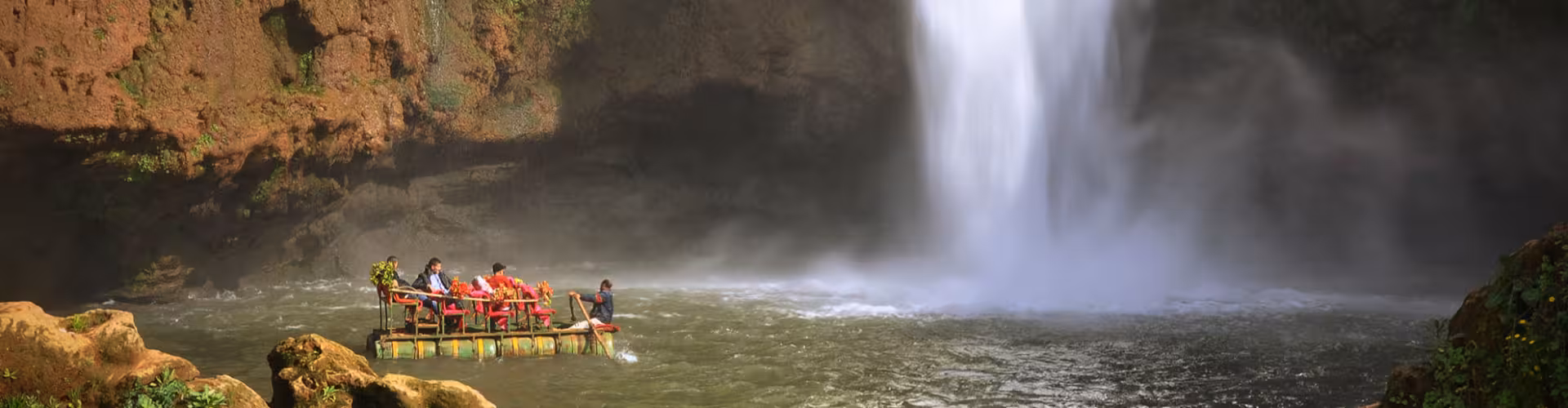 Raft ride at Ouzoud Falls in Morocco with travelers near the powerful waterfall mist, a top Atlas Mountains day trip and hiking attraction.