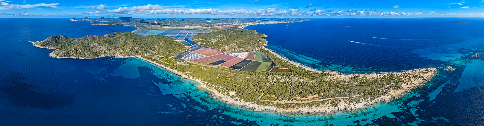 Aerial panorama of Saint George of Ses Salines salt flats and turquoise Mediterranean coastline in Ibiza, showcasing Ses Salines Natural Park beaches and crystal-clear waters.