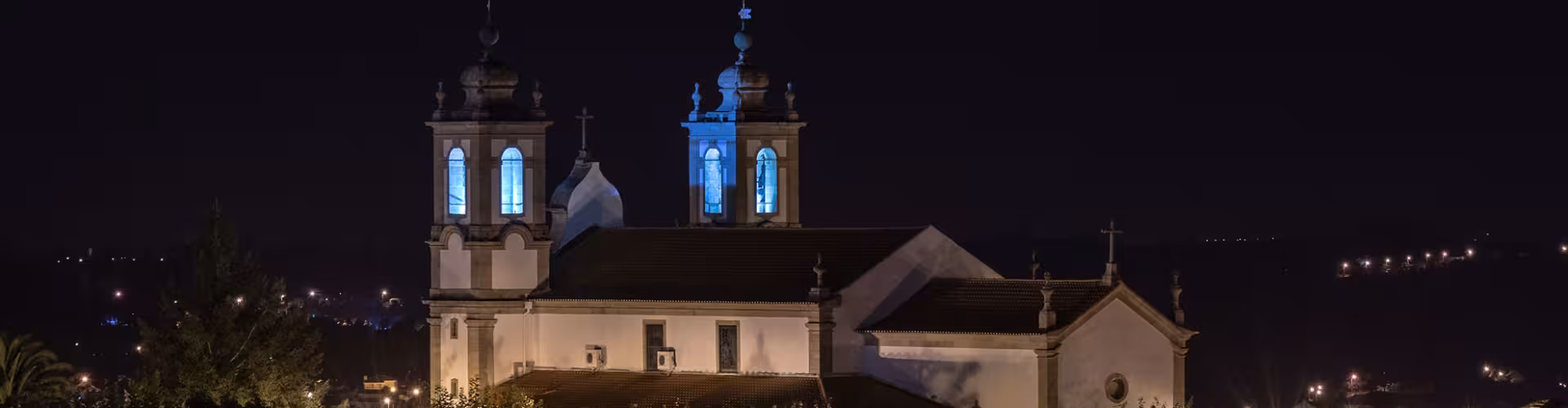 Night view of an illuminated historic church in Seia, Portugal, showcasing its architectural beauty against a serene backdrop.