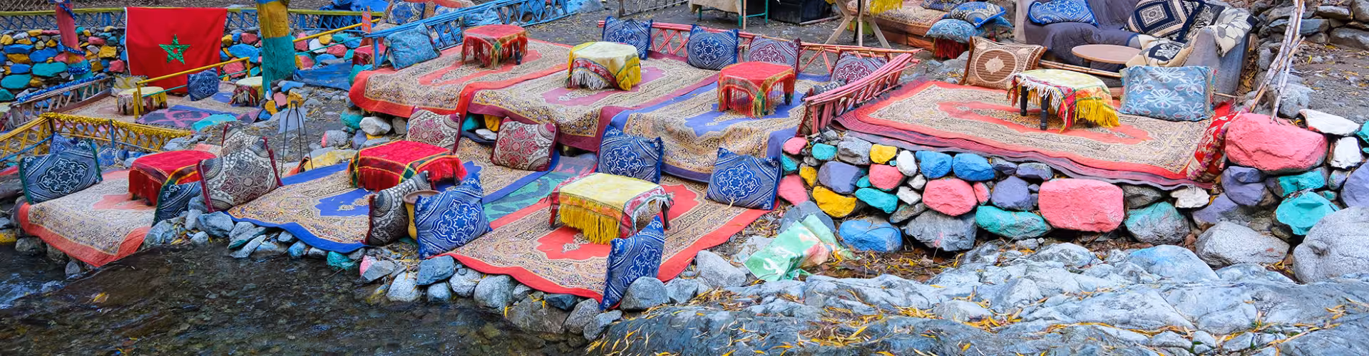 Colorful riverside Berber café seating with Moroccan rugs and cushions in Setti Fadma, Ourika Valley near Marrakech, gateway to the Seven Waterfalls hike