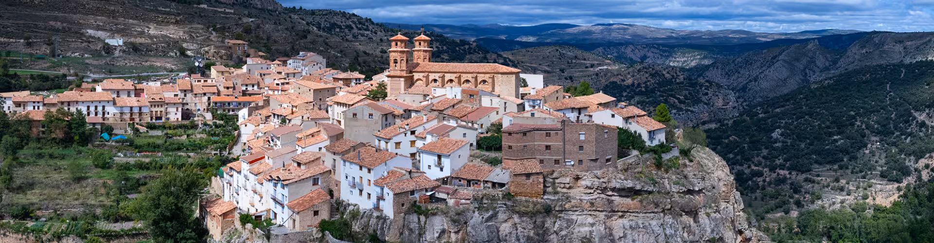 Panoramic view of a cliffside village with terracotta rooftops and a historic church in the rugged landscapes of Teruel, Aragón, Spain.