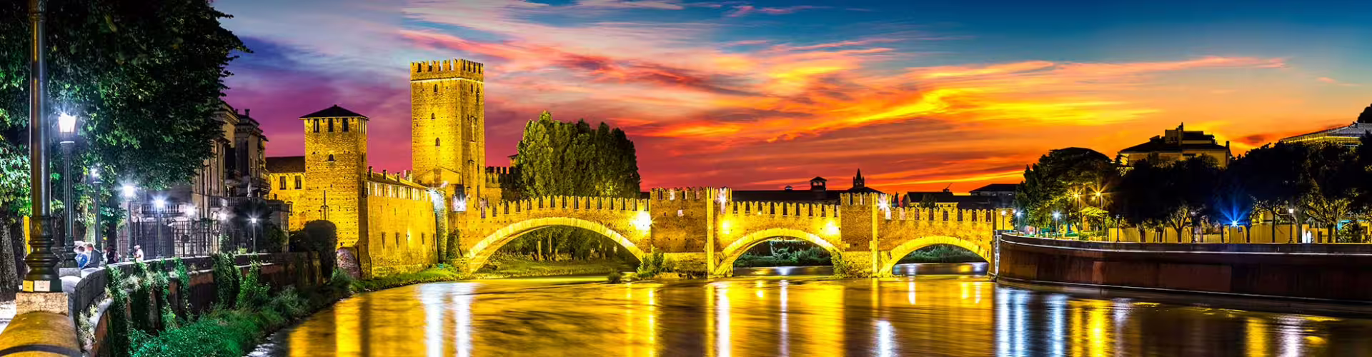 Colorful sunset over Verona's historic Castelvecchio and illuminated bridge reflecting in the Adige River, Italy.