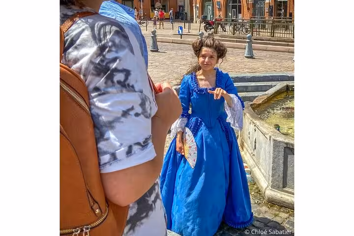 Guide in blue 18th century dress holding a fan during a walking tour in Toulouse