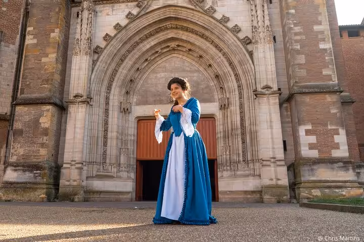 Woman in 18th century blue dress posing before Saint-Étienne Cathedral in Toulouse