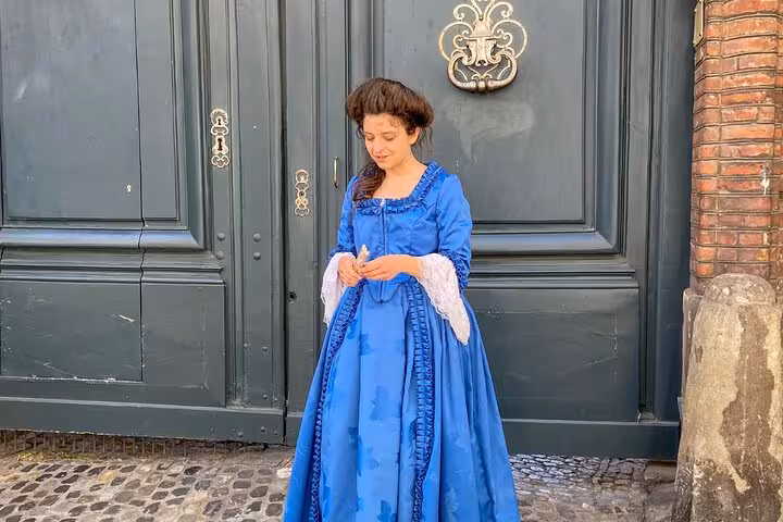 Woman in blue 18th century gown standing before historic door in Toulouse Saint Etienne district