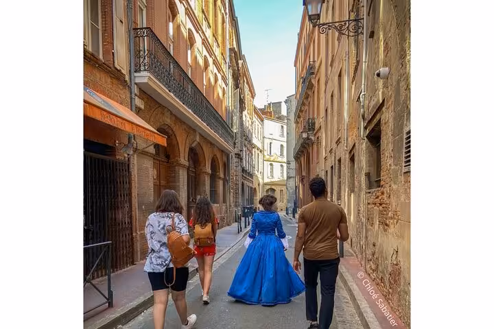 Guide in 18th century blue gown leads visitors through narrow historic streets of Toulouse Saint Etienne district