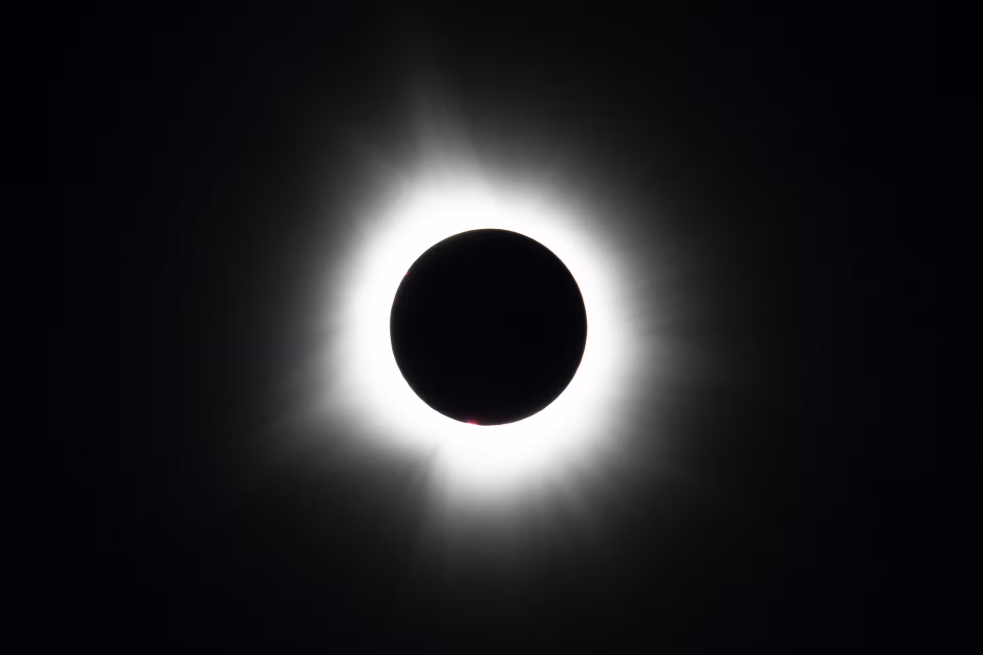 Total solar eclipse with white corona and red prominences visible against black sky