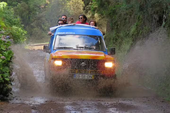 4x4 jeep splashes through muddy trail on a private full-day adventure in Madeira's lush landscapes, offering thrilling off-road fun.