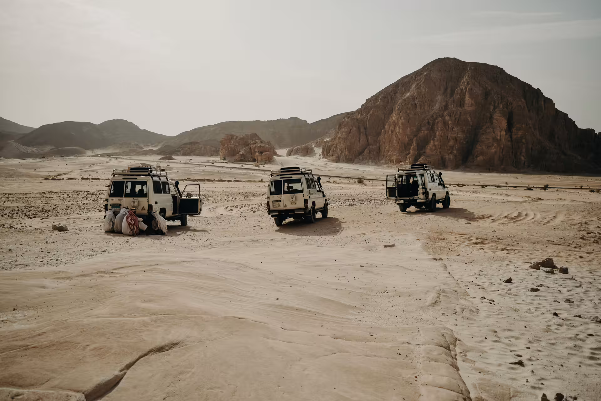 Three white 4x4 jeeps parked in sandy desert landscape with rocky mountains in Marsa Alam, Egypt