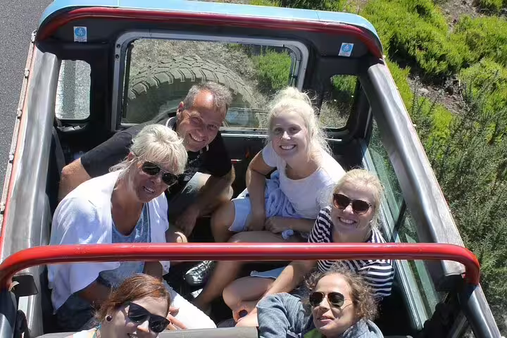 A group of smiling tourists enjoy a scenic 4x4 Jeep adventure through Porto Moniz and Fanal, surrounded by lush greenery.