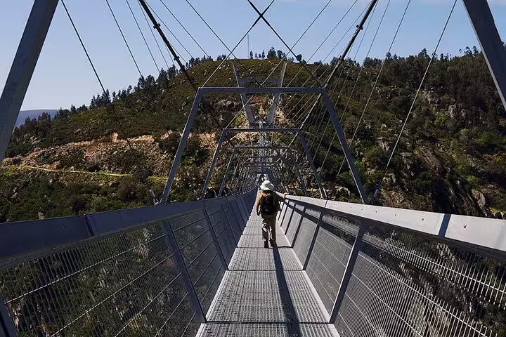 Traveler walking across the 516 Arouca Suspension Bridge surrounded by lush forested hills.