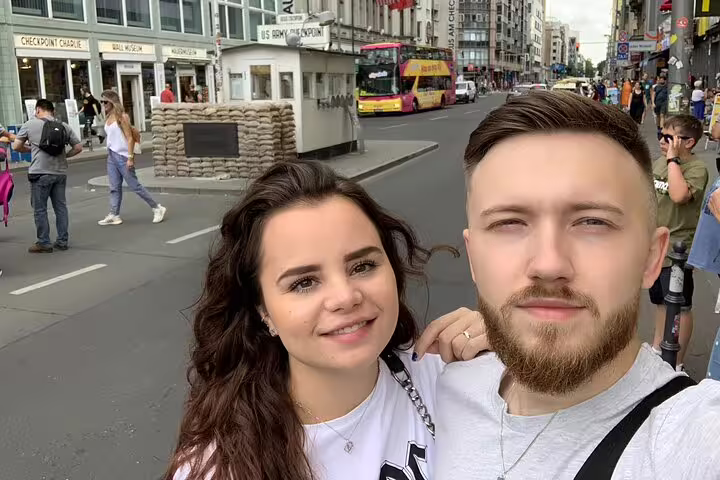 Couple smiling at Checkpoint Charlie landmark on Berlin Wall escape stories self-guided walking tour
