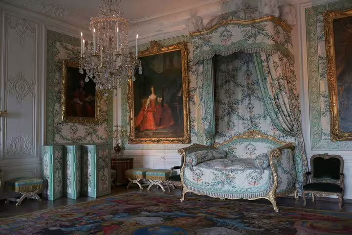 Elegant Versailles room with ornate decor, canopy bed, and royal portraits, part of Paris to Versailles guided tour.