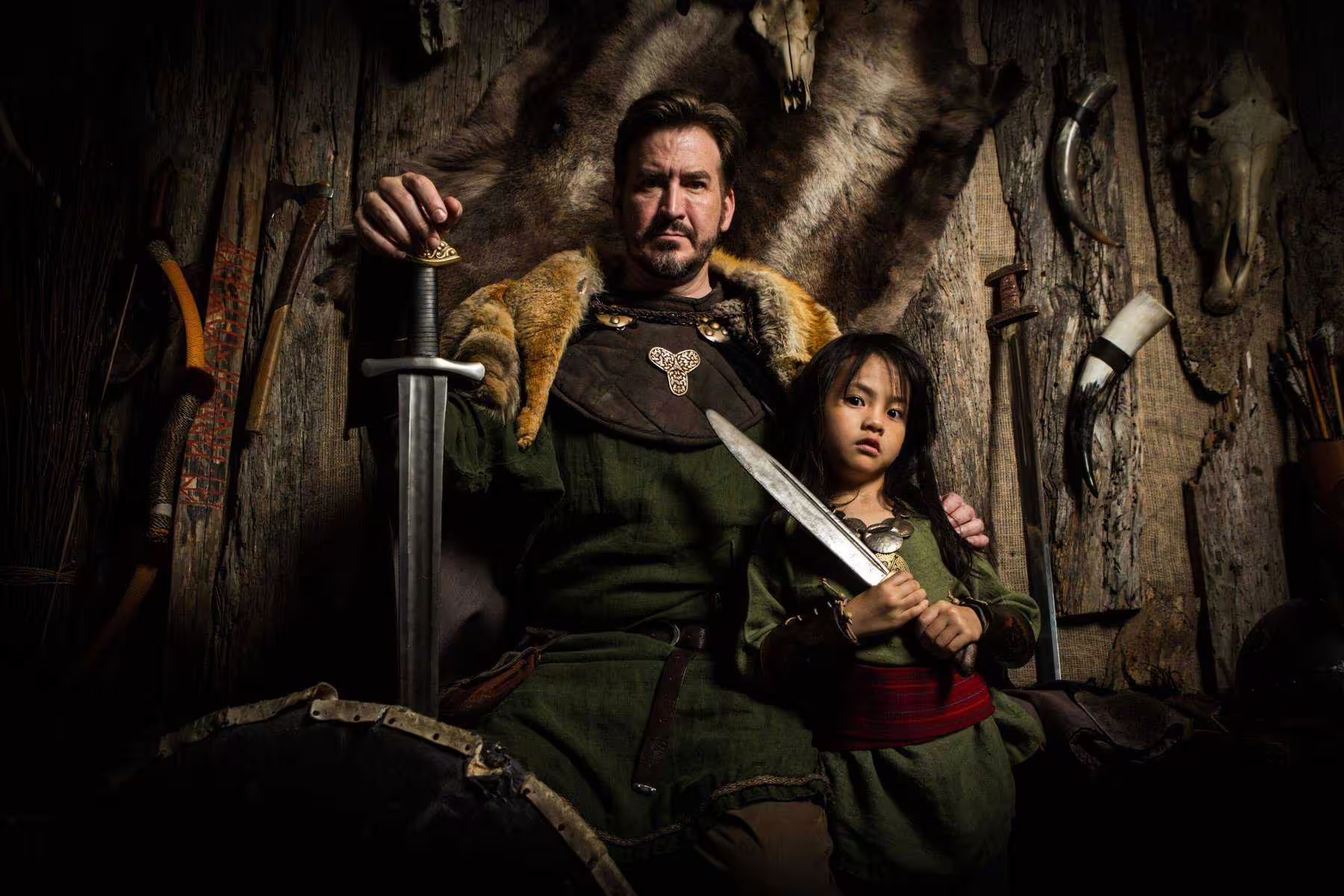 Viking warrior in fur cloak holding sword with child in Norse costume during immersive Iceland saga experience
