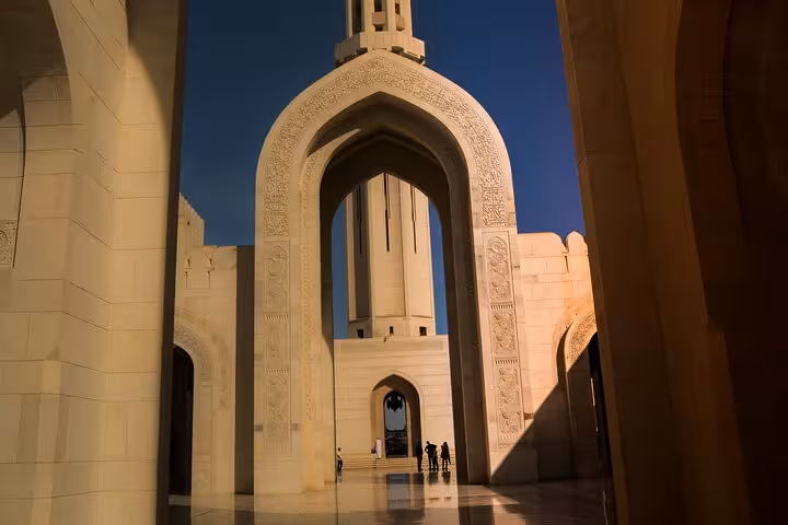 Grand Mosque Muscat intricate archway and minaret glowing at dusk on an evening city tour in Oman