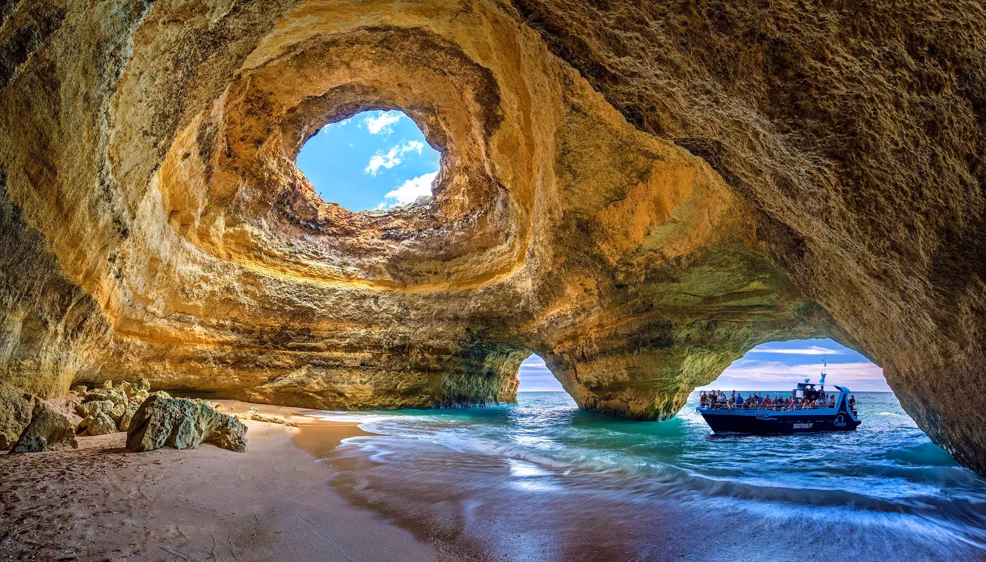Inside view of the iconic Benagil Cave with a boat tour entering through the sea arch, showcasing the natural skylight.